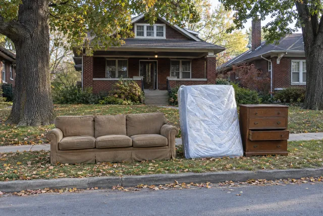 Old couch, wrapped mattress and a dresser set neatly at the curb of a Kansas City brick bungalow, waiting for bulky item pickup