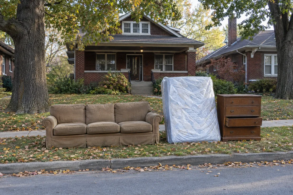 Old couch, wrapped mattress and a dresser set neatly at the curb of a Kansas City brick bungalow, waiting for bulky item pickup